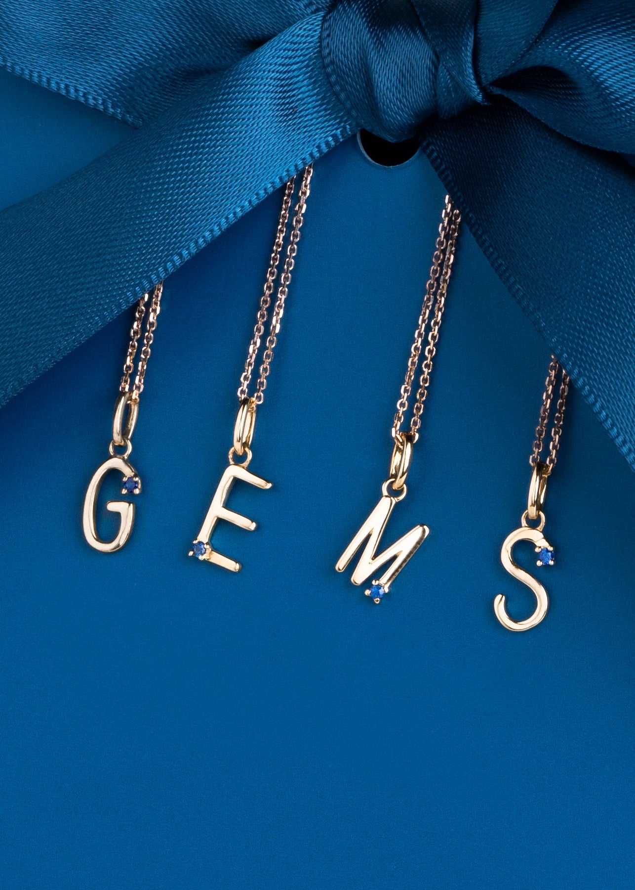 Gold necklaces with 'GEMS' charms on a blue ribbon background